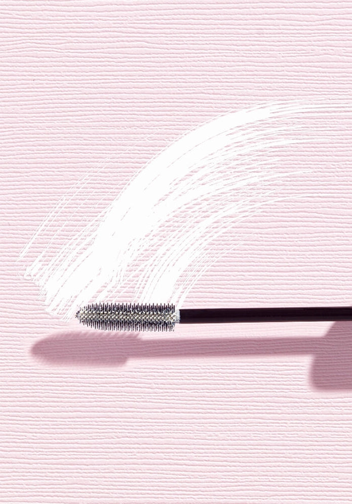 Close-up of mascara primer wand tip with coated bristles on white tube residue