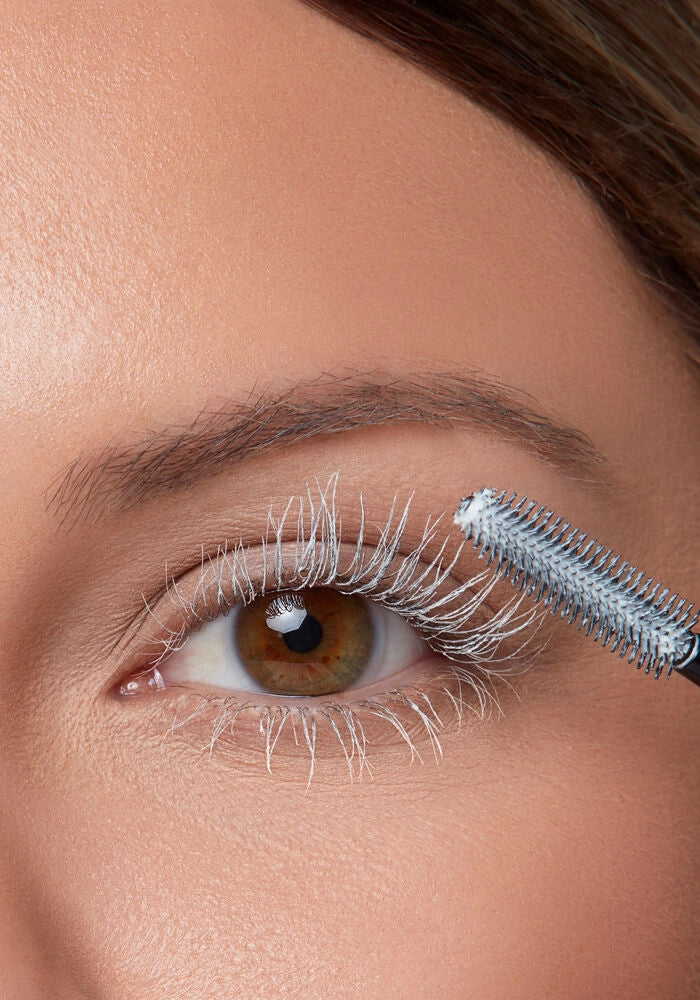 Eye with lashes coated by mascara primer, wand-brush applying visible product