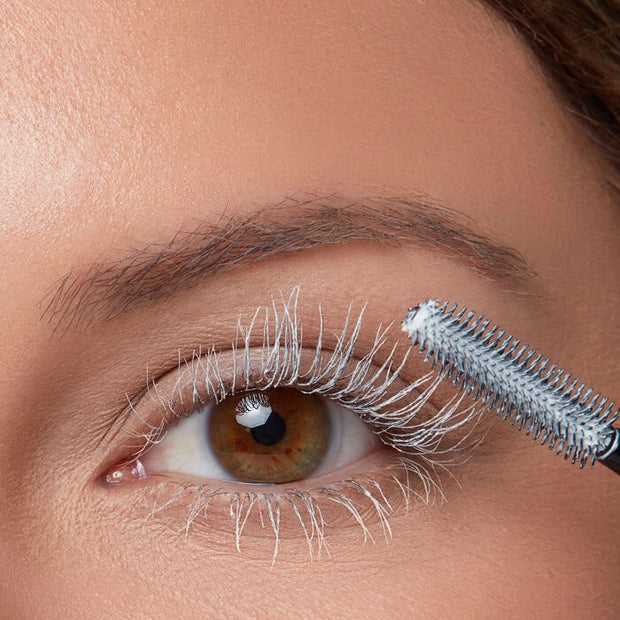 Eye with lashes coated by mascara primer, wand-brush applying visible product