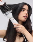 White heated brush styling dark hair with black bristles and rounded barrel head