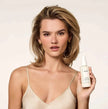 OUAI leave-in conditioner bottle with white pump held near a woman’s shoulder-length hair