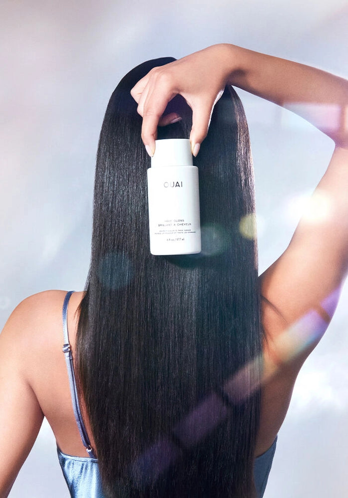 Hair gloss bottle held above long dark hair