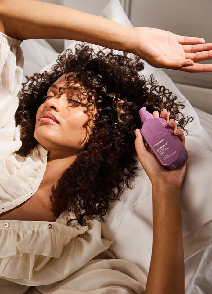 Curly hair being treated with Night.Shift serum bottle, purple