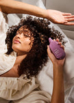 Curly hair being treated with Night.Shift serum bottle, purple