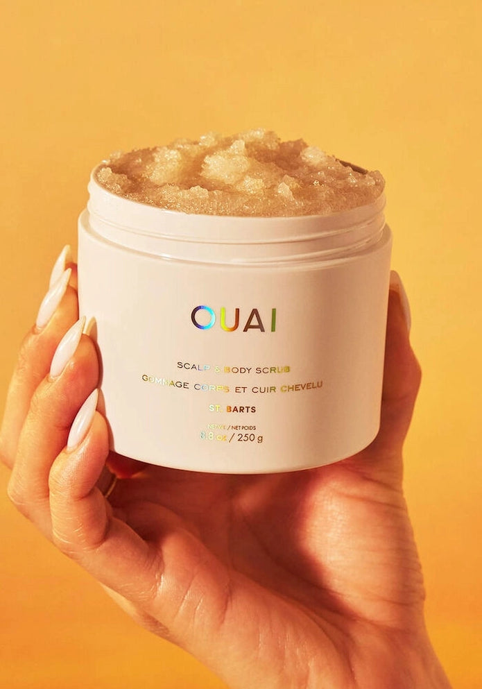 OUAI St. Barts scalp and body scrub jar held in hands, white tub with golden scrub