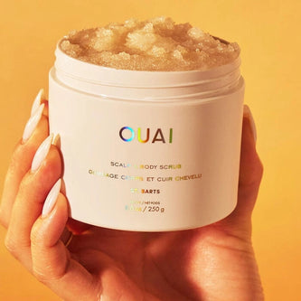 OUAI St. Barts scalp and body scrub jar held in hands, white tub with golden scrub