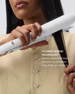 Hands holding a white flat iron to straighten dark hair near the ends