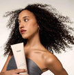 OUAI Curl Crème tube held up by a woman with curly hair