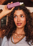 Hand holding UN.TANGLED purple leave-in detangling conditioner bottle with white nozzle